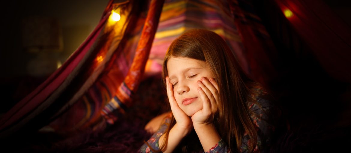 Caucasian girl child dreaming pondered with open eyes in a toy tent with garlands, children's games and houses, dark cozy photo